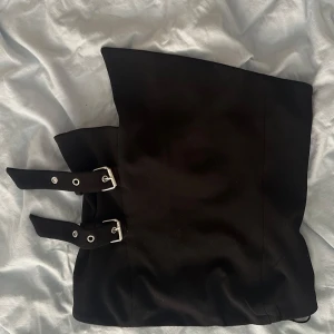 Svart kort tub topp med bälten - Säljer en svart topp med två coola bälten med silvriga spännen framtill. har en rak och stilren form som ger en edgy vibe. Perfekt för dig som gillar minimalistisk stil med en twist. Materialet känns mjukt och följsamt mot huden.