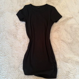Svart ribbad kortklänning - Säljer en svart ribbad kortklänning från Bik Bok. Klänningen har rund halsringning, korta ärmar och en tight passform som framhäver figuren. Perfekt för dig som gillar enkel och stilren design med en modern touch.