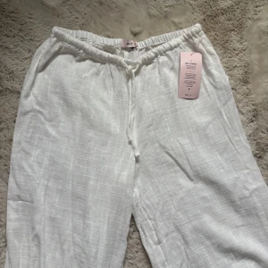 Vita linnebyxor med snörning från Nelly - Snygga vita linnebyxor från Nelly med breda ben och låg midja. Byxorna är helt oanvända med lappen kvar.