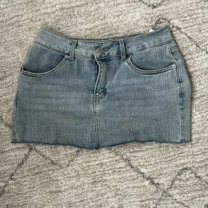 Grå jeanskjol med rå kant - Säljer en grå lågmidjad jeanskjol med klassisk femficksdesign och rå, fransig kant nedtill. 