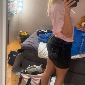 Svart jeanskjol med kontrastsömmar - Säljer en svart jeanskjol med vita kontrastsömmar och klassiska fickor både fram och bak. Kjolen är kort och har en snygg, figurnära passform. 