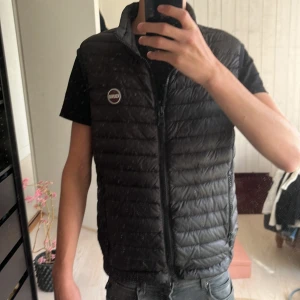 Colmar väst - Säljer en svart dunväst från Colmar Originals med quiltad design och hög krage. Västen har dragkedja framtill, två sidofickor med dragkedja och justerbar dragsko nedtill. Perfekt för lager-på-lager och snygg logga på bröstet. Inga skador som ny typ. Passar mellan 165 till 175 cm lång jag är på bilden 175. Man kan dra åt på insidan på västen så den sitter tajtare, priset är inte hugget i sten så och om ni har några frågor är det bara att fråga.