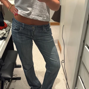 Blå bootcut jeans med låg midja - Snygga blå jeans med bootcut och låg midja, klassisk femficksmodell och coola slitningar. Jeansen har ljus tvätt och kontrastsömmar på bakfickorna. Perfekta för en chill och avslappnad stil. Materialet är jeans i bomull.