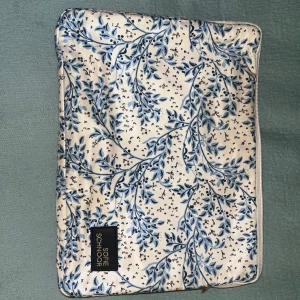 Blommig datorväska från Sofie Schnoor - Snygg datorväska från Sofie Schnoor med blommigt mönster i blått och beige på vit bakgrund. Väskan har dragkedja och är tillverkad i polyester med svart innerfoder. Perfekt för att bära din laptop med stil.