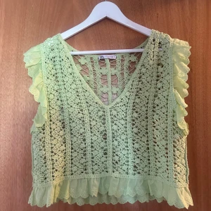 Grön spetsig blus från Zara - Säljer en ljusgrön blus från Zara med v-ringning och volangdetaljer vid axlar och nederkant. Blusen är ärmlös och har ett vackert spetsmönster som ger en bohemisk vibe. Perfekt för dig som gillar unika detaljer och somriga färger.