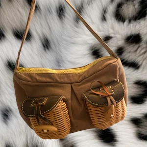 Liten miss sixty väska❤️ - Super söt väska med två korgflätade fickor❤️ den är en liten väska man kan ha i handen❤️den är 27cm bred och 17 cm lång, hela bandet är 42 cm 