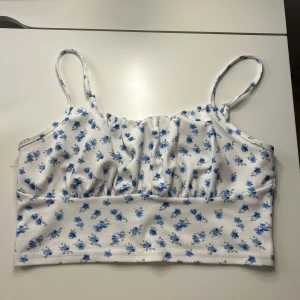 Vit blommig linnetopp från SHEIN - Supersöt vit linnetopp från SHEIN med blå små blommor över hela tyget. Toppen har smala axelband och en lätt rynkad front för extra chill vibe. Materialet är mjuk polyester med lite stretch för skön passform. Perfekt för varma dagar och sommarhäng.