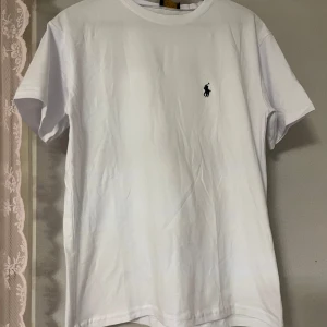 Vit t-shirt från Polo Ralph Lauren - Vit t-shirt från Polo Ralph Lauren med klassisk rund hals och korta ärmar. Diskret broderad logga i marinblått på bröstet. T-shirten är gjord i mjuk bomull och har en clean, stilren look som funkar till allt. Perfekt basic för garderoben.