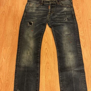 Dsquared2 Herr storlek 48 - Snygga blå jeans från Dsquared2 i skinny fit med slitningar, färgstänk och coola detaljer. Klassisk femficksmodell med låg midja och raka ben. Tillverkade i bomull med en schysst tvättad look och patch bak i midjan. Perfekta för dig som gillar streetstyle och vill sticka ut.