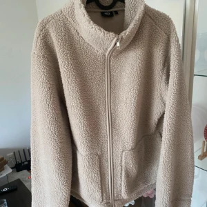 Beige teddyjacka med dragkedja - Mysig teddyjacka i beige från 157, med hög krage och sned dragkedja framtill. Jackan har två stora fickor och är tillverkad i fluffigt fleece-material som ger en chill och avslappnad vibe. Perfekt för kalla dagar när du vill vara både varm och snygg. Knappt använd då den beige färgen inte passade mig🥲 det är storlek L men jag är S/m och tycker den passar mig bra