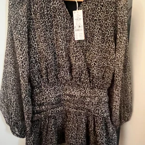 Leopardmönstrad kortklänning med v-ringning - Säljer denna helt oanvända klänningen från Gina med prislappen kvar. Klänningen är v ringad i leopard mönster och har även små tunna guld ränder som ni kan se tydligare på bild 3🫶🏼den är i storlek 158/164 men passar även mig som vandligtvist har xs/s. Den är ganska kort i modellen och v ringningen går även att göra djupare om man tar bort fästet som håller ihop den🫶🏼🫶🏼