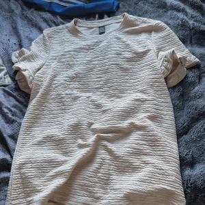 Beige ribbad t-shirt från SHEIN - Snygg beige t-shirt från SHEIN i storlek S. T-shirten har korta ärmar med volangdetalj och ett ribbat, vågigt tyg som ger en cool struktur. Perfekt för dig som gillar neutrala färger och vill ha något som sticker ut lite i garderoben, Och hålla sthlm stilen.