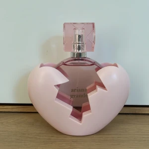 Ariana Grande parfym med hjärtfodral - Säljer en Ariana Grande parfym i en rund, rosa glasflaska med transparent rosa lock. Flaskan kommer med ett ljusrosa hjärtfodral med ett krossat hjärta-design. Volymen är 100 ml Eau de Parfum. Aldrig använd🩷