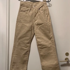Beige raka jeans med hög midja - Snygga beige jeans med rak passform och hög midja. Klassisk femficksmodell med knapp och dragkedja framtill. Perfekta för dig som gillar en clean och enkel stil. Materialet är mjukt och känns skönt mot huden.