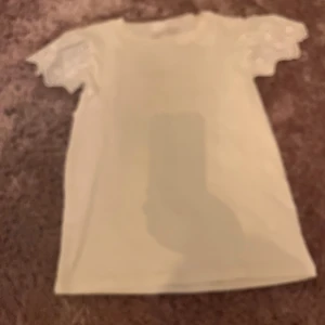 Vit t-shirt med spetsärmar från Gina tricot - Säljer en söt vit t-shirt från Gina tricot young i storlek 158/164. T-shirten har korta ärmar med fina spetsdetaljer som ger en extra touch. Perfekt för dig som gillar stilrena plagg med lite extra detaljer. Materialet känns mjukt och skönt mot huden.