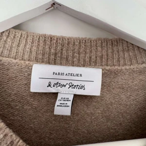 Beige stickad tröja från & Other Stories - Snygg beige stickad tröja från & Other Stories Paris Atelier i storlek XS. Tröjan har en rund hals, långa ärmar och breda ribbade muddar vid ärmslut och nederkant. Perfekt för lager-på-lager och chill stil under höst och vinter.