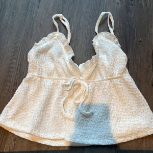 Vit linnetopp med volang från SHEIN - Supersöt vit linnetopp från SHEIN med volangdetaljer vid axelbanden och v-ringad hals. Toppen har knyt framtill och är tillverkad i ett krispigt, strukturerat polyestertyg med lite stretch. Perfekt för sommarens alla häng och chill.