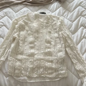 Vit spetsblus från Zara - Säljer en elegant vit spetsblus från Zara med vackra detaljer och långärmad design. Perfekt för en stilren look. Blusen har ett intrikat mönster och är tillverkad i ett lätt och luftigt material.