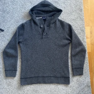 Grå hoodie från Oscar Jacobson - Säljer en stilren grå hoodie från Oscar Jacobson. Tröjan har en ribbad kant vid ärmslut och nederkant samt knappar vid halsen för extra stil. Perfekt för kyliga dagar. Skriv vid frågor