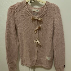 Odd Molly Rosa stickad kofta med rosetter - Säljer en söt rosa stickad kofta från OZ med dekorativa rosetter framtill. Koftan har långa ärmar och ribbstickade kanter. Perfekt för kyliga dagar! St 1