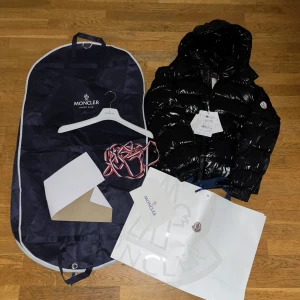 Moncler Maya inklusive originalförpackning  - Säljer en snygg svart dunjacka från Moncler. Jackan har en glansig finish och är utrustad med dragkedja. Perfekt för kyligare väder och ger en stilren look. Kommer med originalpåse och galge.