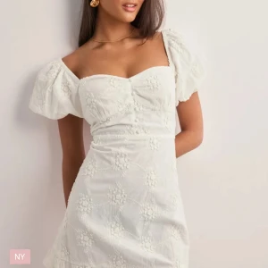 Vit blommig klänning - Charmig vit klänning med blommigt mönster och puffiga kortärmar. Den har en söt volangdetalj vid fållen och en smickrande passform. Perfekt för somriga dagar.