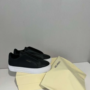 Svarta sneakers från Axel Arigato - Stilrena svarta sneakers från Axel Arigato med en minimalistisk design. Skorna har en vit platåsula och är tillverkade i skinn. Perfekta för en modern och avslappnad look. Den är helt ny eftersom den va för liten. Allt kommer skickas med. 