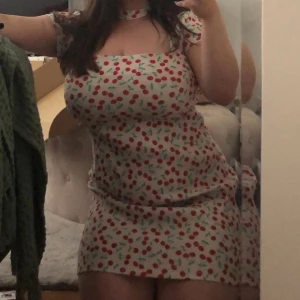 Vit klänning med körsbärsmönster - Söt vit klänning med körsbärsmönster i rött och grönt. Klänningen har korta ärmar och en söt knäppning i nacken. Något nopprig på ett ställe och ett av banden sticker ut lite (se bilder) 