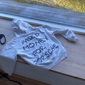 Vit hoodie med tryck - Säljer en vit hoodie med texten 'Need Money for Porsche' tryckt på ryggen. Tröjan har en klassisk design med huva och långa ärmar. Perfekt för en avslappnad stil.