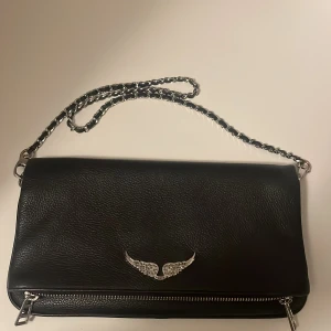 Svart zadig Voltaire väska med kedja - Snygg svart axelväska i skinn från Zadig & Voltaire i bra skick. Väskan har den klassiska dekorativa vingdetalj i silver. Sparsamt andvänd. 
