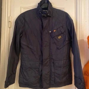 Mörkblå jacka från G-Star RAW - Säljer en mörkblå jacka från G-Star RAW med dragkedja och knappar framtill. Jackan har flera praktiska fickor och en hög krage. Perfekt för höst och vår.