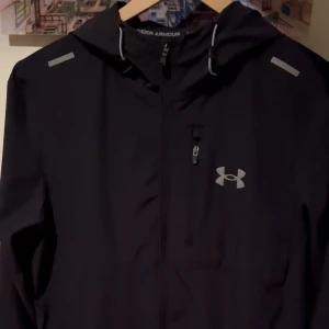 Svart Vanish Jacket från Under Armour - Snygg svart vindjacka från Under Armour med luva.                                                                                  Skick: 9,9/10 använd under 10 gånger och nyligen köpt.                                                                    Storlek: S men kan se slapping ut, passar bäst på någon med storlek M