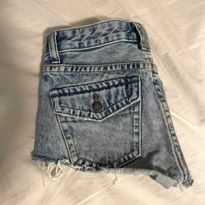 Lågmidjade jeansshorts från Pull&Bear - Snygga blå jeansshorts från Pull&Bear med fransiga kanter och slitna detaljer. Perfekta för en avslappnad sommarlook. De har en klassisk femficksdesign och knappgylf. Super bra till sommaren.