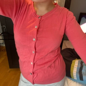 Rosa kofta med knappar - Säljer en söt rosa kofta med knappar framtill. Den har långa ärmar och en rund halsringning. Perfekt för att lägga till en färgklick i din garderob! Merket ar Noa Noa