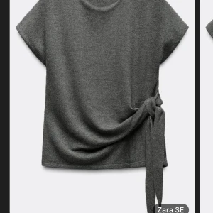 Grå topp från Zara med knyt - Snygg grå topp från Zara med korta ärmar och en stilren knytning i sidan. Perfekt för en avslappnad men chic look. Passar bra till både jeans och kjol.