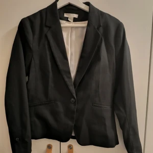 Svart kavaj från H&M - Snygg svart kavaj från H&M i storlek 38. Kavajen har en klassisk design med en knapp framtill och två fickor. Perfekt för en stilren look.