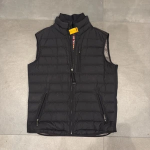 Svart dunväst från Parajumpers - Säljer en stilren svart dunväst från Parajumpers. Västen har en dragkedja framtill och två praktiska fickor med dragkedjor. Perfekt för lager-på-lager under kyliga dagar Den har ett litet hål vid vänster ficka som knappt är synligt och små smutsfläckar som jag borde kunna ta bort med vatten innan köp. Nypris 3299kr