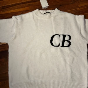 Vit tröja från Cole Buxton - Säljer en stilren vit tröja från Cole Buxton med svarta initialer 'CB' på bröstet. Tröjan har en klassisk rund hals och är tillverkad i ett mjukt material som ger en bekväm passform. Perfekt för en avslappnad look.