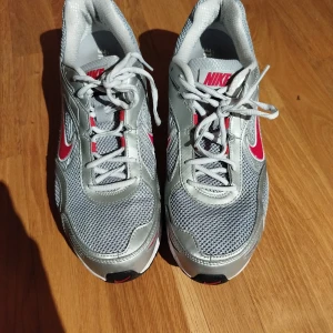 Nike sneakers Alaris 4 - Snygga Nike sneakers i silver med röda detaljer och vit sula. Skorna har snörning och en sportig design med meshmaterial för bra andningsförmåga. Perfekta för träning eller en aktiv vardag.