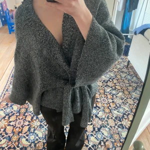 Grå stickad kofta med knytband - Mysig grå stickad kofta med ett knytband i midjan. Koftan har en lös passform och långa ärmar.