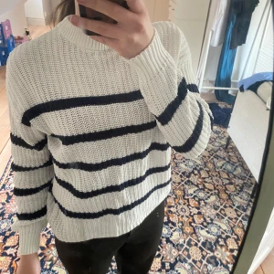 Vit och marinblå randig stickad tröja - Säljer en vit stickad tröja med marinblå ränder. Tröjan har en rund hals och långa ärmar.