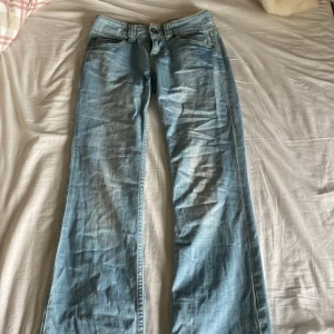 Ljusblå jeans från Hilfiger Denim  - Snygga ljusblå jeans från Hilfiger Denim med klassisk femficksdesign. De är utsvängda och lågmidjade och är tillverkade i jeansmaterial. Perfekta för en avslappnad stil. Säljer för de har blivit för små. Innebenslängd 77cm och över midjan 35cm