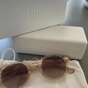 Solglasögon från Chimi - Snygga solglasögon från Chimi med transparent beige båge och runda, mörka linser. Perfekta för en stilren look. Helt nya och oanvända. Man får med påsen och fodralet som låg i☀️