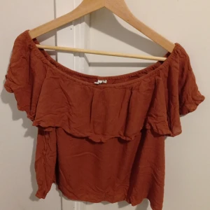 Terracotta offshoulder topp från NLY Trend - Säljer en snygg terracotta offshoulder topp från NLY Trend. Toppen har volangdetaljer och en luftig passform, perfekt för varma dagar. Den är tillverkad i ett lätt och bekvämt material. Skriv gärna om du vill ha mer information om toppen 