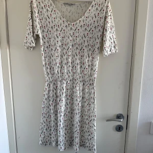 Vit blommig klänning från 157 - Charmig vit klänning med blommigt mönster från 157. Den har en v-ringad hals och trekvartsärmar, (katt och kanin finns i hemmet) 