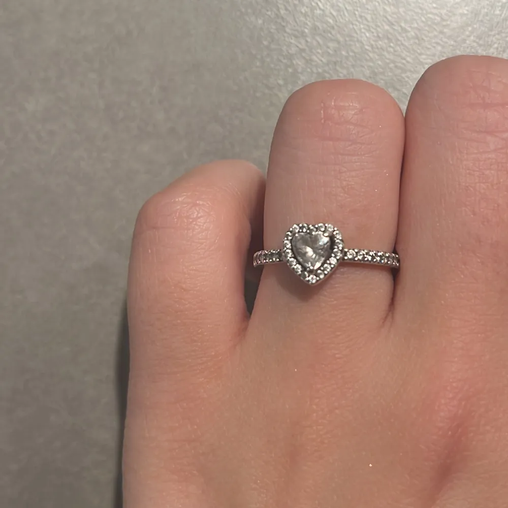 Elegant silverring från Pandora med en gnistrande hjärtformad sten i mitten, omgiven av små glittrande stenar. Perfekt för att ge en romantisk touch till någon du gillar eller till dig själv!!!. Asusteet.