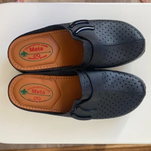 Svarta perforerade tofflor från Meta - Säljer ett par svarta perforerade tofflor från Meta. De har en bekväm passform . Perfekta för inomhusbruk eller som arbetsskor. Tillverkade i syntetmaterial med en slitstark sula. Märkt storlek 41 men passar 39 perfekt 