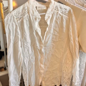 Vit blus från Rosemunde Copenhagen - Säljer en elegant vit blus från Rosemunde med spetsdetaljer på axlarna och längs sidorna. Blusen har långa ärmar och en klassisk krage. Perfekt för en stilren look. Aldrig använd.