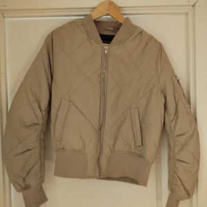 Beige bomberjacka från Price Kate - Säljer en snygg beige bomberjacka från Price Kate i storlek 36. Jackan har en quiltad design med dragkedja framtill och långa ärmar. Perfekt för en stilren look.