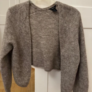 Beige stickad kofta från Lindex - Mysig beige stickad kofta från Lindex i storlek XS. Koftan har en croppad design och långa ärmar, perfekt för kyliga dagar. Den är tillverkad i ett mjukt material som ger en skön känsla. Ett stilrent plagg som passar till många olika outfits.